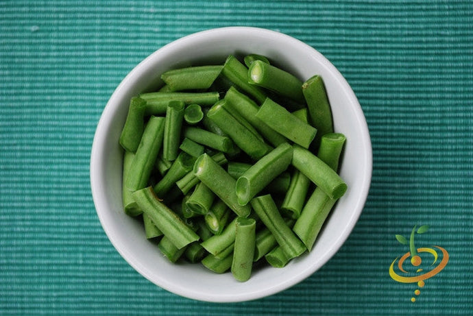 Chopped Tendergreen Bush Bean pieces in a white bowl on a green textured surface