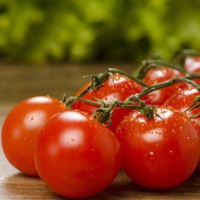 Fresh red cherry tomatoes on the vine with water droplets on a wooden surface